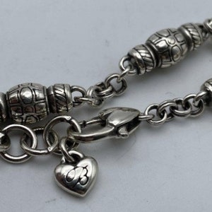 May include: A silver charm bracelet with a heart charm and a clasp. The bracelet has a chain with small round links and decorative beads.