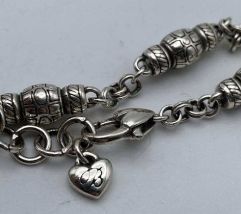 May include: A silver charm bracelet with a heart charm and a clasp. The bracelet has a chain with small round links and decorative beads.