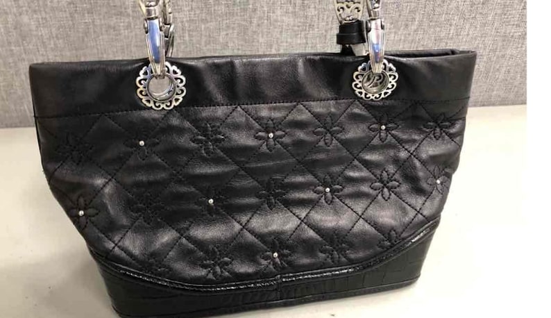 Pu&ograve; includere: Borsa tote in pelle nera con dettagli in argento e un design trapuntato con piccoli accenti floreali.