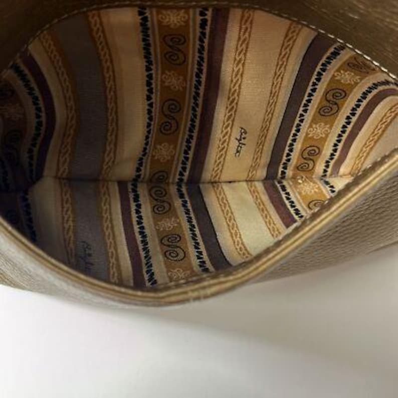 May include: A close-up view inside a tan-colored handbag. The interior lining features a patterned design with vertical stripes in shades of brown, beige, and cream. The bag's outer material has a textured appearance. The brand name is visible on the lining.