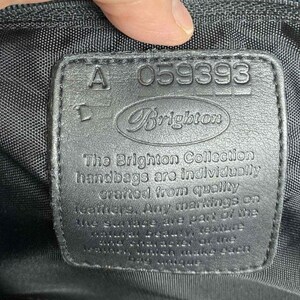 K&ouml;nnte beinhalten: Ein schwarzes Leder-Etikett mit dem Text "A-059393 Brighton" und dem Text "The Brighton Collection handbags are individually crafted from quality leathers. Any markings on the surface are part of the natural beauty of the leather and will make each bag unique."