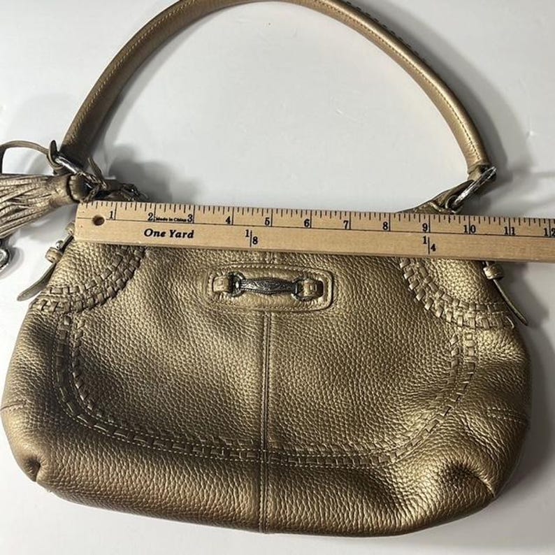 May include: A metallic gold handbag with a top handle and a decorative tassel. The bag has a textured surface and decorative stitching along the edges. The bag measures approximately 12 inches in length.