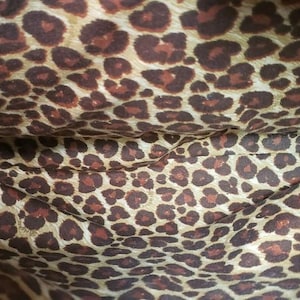 May include: Interior of a bag with a leopard print pattern. The fabric is a light tan color with dark brown spots. The pattern is repeated throughout the lining of the bag.