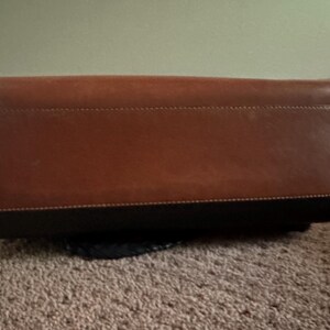 May include: A brown leather handbag with a black base. The bag has a rectangular shape with a stitched seam detail. The leather has a smooth texture and a rich, warm color.