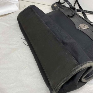 K&ouml;nnte beinhalten: Schwarze Tragetasche mit geflochtenem Riemen und einer silbernen Schnalle. Die Tasche ist aus strapazierf&auml;higem Stoff und hat einen Lederbesatz.