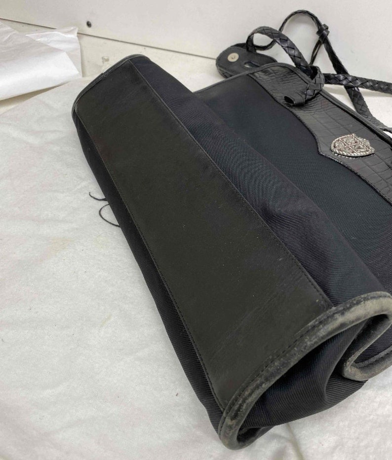 K&ouml;nnte beinhalten: Schwarze Tragetasche mit geflochtenem Riemen und einer silbernen Schnalle. Die Tasche ist aus strapazierf&auml;higem Stoff und hat einen Lederbesatz.