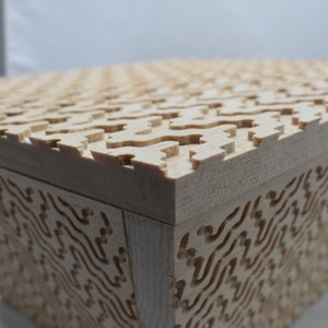May include: A wooden box with a geometric pattern on the top and sides. The box is made of light wood and has a natural finish.