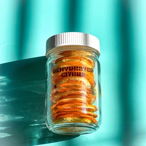 Pode incluir: Um frasco de vidro cheio de fatias de laranja desidratadas. O frasco tem uma tampa branca e um rótulo que diz "Citrus desidratado Laranjas".