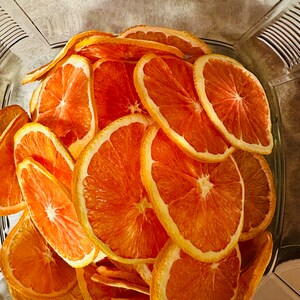 May include: A clear glass container filled with dried orange slices. The orange slices are a vibrant orange color with a yellow rind. The slices are arranged in a slightly overlapping pattern, creating a visually appealing display.