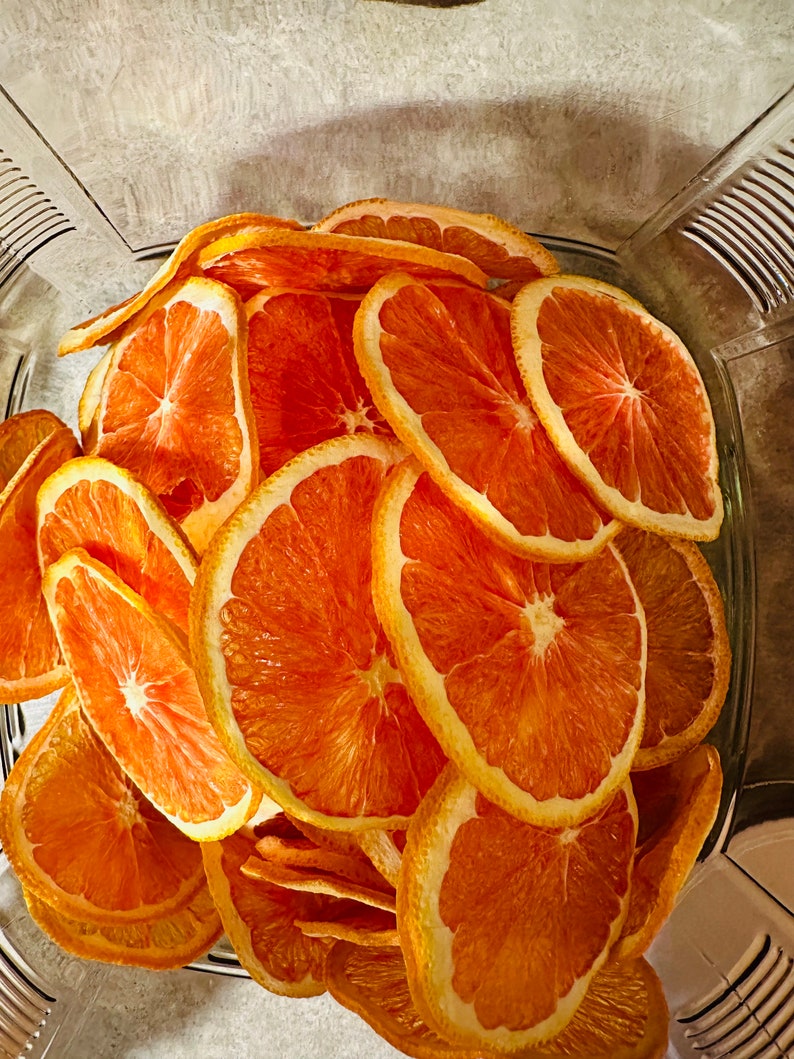 May include: A clear glass container filled with dried orange slices. The orange slices are a vibrant orange color with a yellow rind. The slices are arranged in a slightly overlapping pattern, creating a visually appealing display.