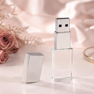 Puede incluir: Una unidad flash USB de acrílico transparente y plateado con un cuerpo rectangular y una tapa plateada extraíble a juego. La unidad cuenta con un conector metálico en la parte superior y una base transparente, con un diseño limpio.