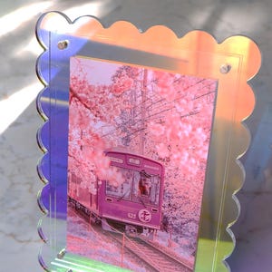 Könnte beinhalten: Dekorativer Fotorahmen mit gewelltem Rand und schillerndem Finish. Der Rahmen enthält ein Bild eines lila Zuges, der durch rosa Kirschblüten fährt. Der Zug hat die Nummer 623.