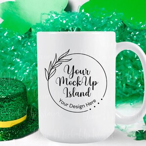 May include: White ceramic mug with a black design that says "Your Mock Up Island" and "Your Design Here". The mug is surrounded by green tissue paper and shamrocks.