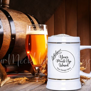 Könnte beinhalten: Ein weißer Keramik-Bierkrug mit goldfarbenem Rand und einer schwarz-weißen Grafik mit der Aufschrift "Your Mock Up Island" und "Your Design Here". Der Krug steht auf einem Holztisch mit einem Bierglas und einem Holzfass im Hintergrund.