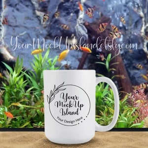 May include: White ceramic mug with a black circle design featuring the text "Your Mock Up Island" and "Your Design Here". The mug is sitting on a light brown surface in front of a fish tank with green plants and colorful fish.