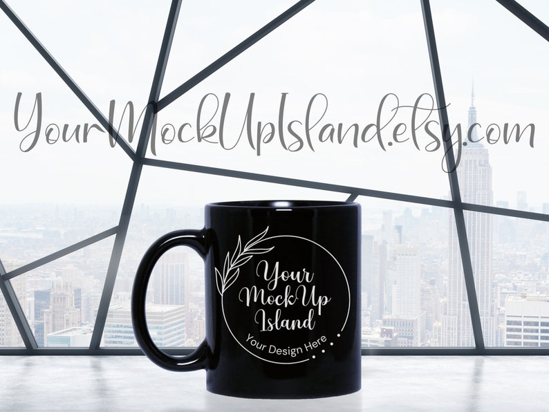 Może przedstawiać: Czarny kubek ceramiczny z białym wzorem, na kt&oacute;rym widnieje napis "Your Mock Up Island" i "Your Design Here". Kubek stoi na białym blacie przed oknem z widokiem na miasto.
