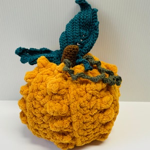 May include: A crocheted pumpkin with a fuzzy orange texture and a green and blue crocheted stem and leaves.