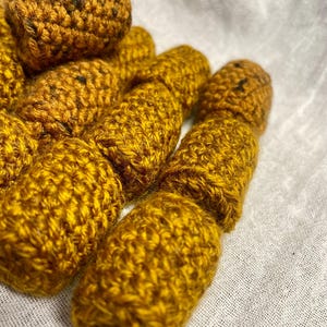 May include: A group of crocheted brown and gold yarn rolls. The rolls are made with a textured stitch and have a slightly fuzzy appearance.