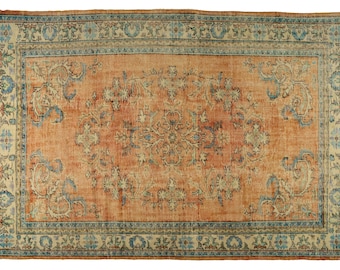 May include: A vintage rug with a floral pattern in shades of orange, blue, and cream. The rug has a central medallion and a border with repeating motifs.