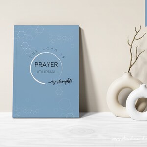 May include: A blue prayer journal with a white circle and the text "The Lord is Prayer Journal...my strength!"  The background has a geometric pattern.