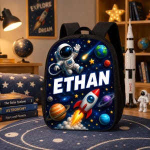 May include: A black backpack featuring a vibrant space-themed print with an astronaut, a rocket ship, planets, and stars. The name ETHAN is printed in large white capital letters across the center of the bag, which has black straps and side pockets.