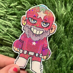 Pu&ograve; includere: Un adesivo con un personaggio dei cartoni animati in un costume da supereroe rosso e rosa con una stella sul petto e sulla testa. Il personaggio ha una barba bianca, una maschera e un'espressione sorridente. L'adesivo ha una finitura glitterata.