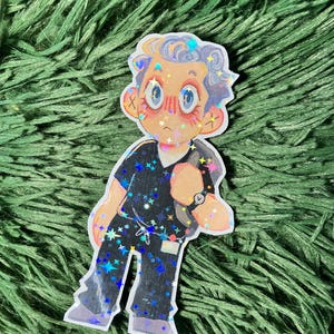 K&ouml;nnte beinhalten: Ein Aufkleber mit einer Cartoon-Illustration einer Person in schwarzer Arbeitskleidung mit einer Uhr. Die Arbeitskleidung ist mit holografischen Sternen verziert. Die Person hat helle Haut, blaue Augen und hellgraues Haar. Der Aufkleber befindet sich auf einem gr&uuml;nen, strukturierten Hintergrund.
