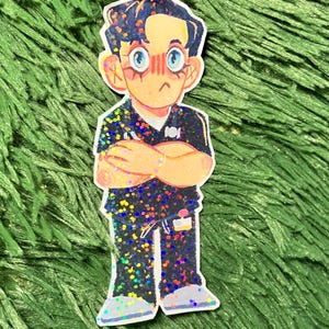 K&ouml;nnte beinhalten: Ein Aufkleber mit einer Cartoon-Illustration einer Person mit verschr&auml;nkten Armen. Die Figur hat dunkles Haar, blaue Augen und ein ger&ouml;tetes Gesicht. Die Kleidung ist schwarz mit bunten Glitzerakzenten. Der Aufkleber befindet sich auf einem gr&uuml;nen, strukturierten Hintergrund.