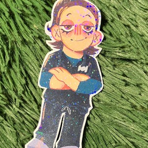 K&ouml;nnte beinhalten: Aufkleber mit einer Cartoon-Illustration einer Person mit verschr&auml;nkten Armen. Die Figur hat braune Haare, ein blaues und schwarzes Outfit und einen l&auml;chelnden Gesichtsausdruck. Der Aufkleber hat einen glitzernden, holografischen Effekt.