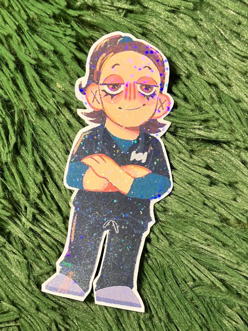 K&ouml;nnte beinhalten: Aufkleber mit einer Cartoon-Illustration einer Person mit verschr&auml;nkten Armen. Die Figur hat braune Haare, ein blaues und schwarzes Outfit und einen l&auml;chelnden Gesichtsausdruck. Der Aufkleber hat einen glitzernden, holografischen Effekt.