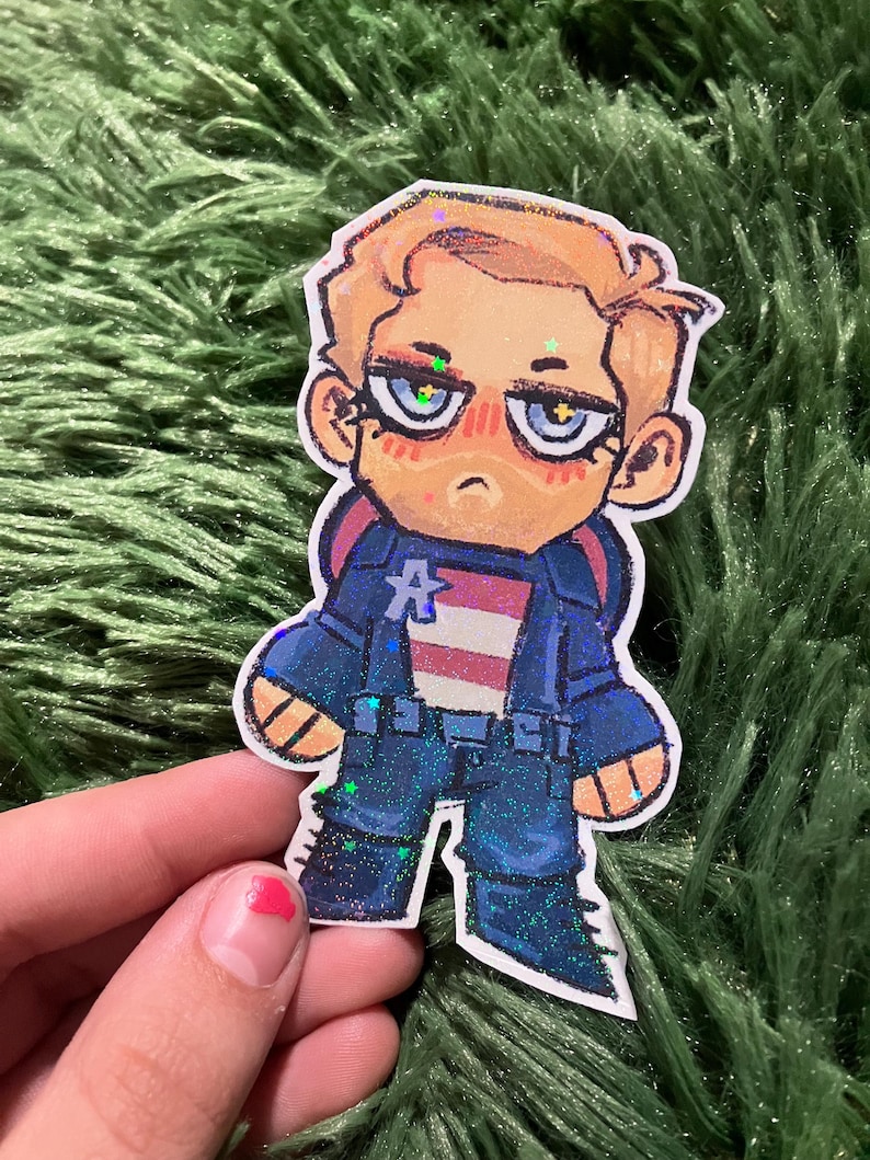 Pu&ograve; includere: Un adesivo con un'illustrazione a cartoni animati di Capitan America. Il personaggio indossa un'uniforme blu con il petto a strisce bianche e rosse. L'adesivo ha accenti glitterati.