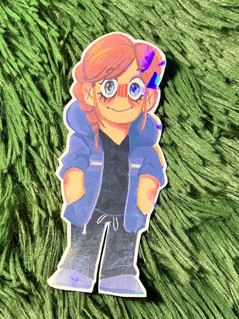 K&ouml;nnte beinhalten: Ein Aufkleber mit einer Cartoon-Illustration einer Person mit roten Haaren, blauen Augen und einer blauen Jacke. Die Figur tr&auml;gt ein schwarzes Hemd und eine graue Hose. Der Aufkleber hat ein holografisches Finish.
