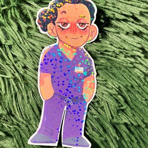 K&ouml;nnte beinhalten: Ein Aufkleber mit einer Cartoon-Illustration einer Person in lila Arbeitskleidung. Die Figur hat dunkles Haar mit bunten Glitzerakzenten, rosigen Wangen und einem kleinen Namensschild. Die Arbeitskleidung ist mit schillerndem Glitzer bedeckt.