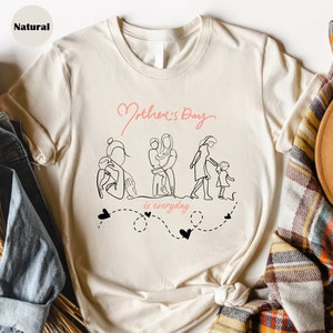 May include: A cream-colored t-shirt with the words "Mother's Day" in pink script above a line drawing of a mother and child. The phrase "is everyday" is below the drawing in pink, with black hearts.
