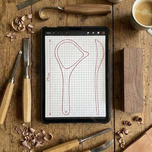 May include: A collection of woodworking tools, including chisels, a hook knife, and a tablet displaying a 29 cm design. A cup of coffee and wood wax are also present on a wooden surface, suggesting a craft project.