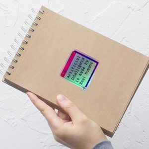 May include: A brown notebook with a spiral binding and a holographic sticker that says "Artificial Intelligence is made by Real Humans".