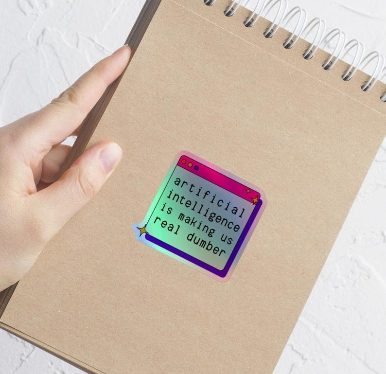May include: A holographic sticker with the text "artificial intelligence is making us real dumber" in a retro computer window design. The sticker has a gradient of pink, purple, and blue colors.