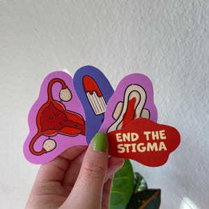 Könnte beinhalten: Drei Aufkleber mit Illustrationen der weiblichen Anatomie und dem Spruch "End the Stigma" in weißer Schrift auf rotem Hintergrund.