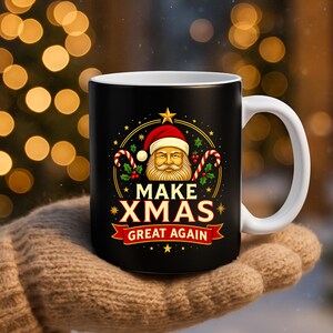 May include: Black ceramic mug with a white handle featuring a Santa Claus design. The mug has the text "MAKE XMAS GREAT AGAIN" in red and gold, with candy canes and stars. The mug is held by a person wearing a brown glove.