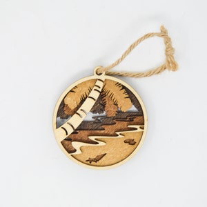 May include: A wooden ornament featuring a palm tree silhouette with a brown and tan wood grain pattern. The ornament is round and has a twine hanger.