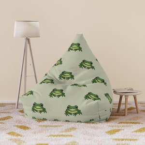 May include: A light green bean bag chair with a repeating pattern of cartoon frogs. The frogs are green with black outlines and white eyes. The bean bag is in a room with a floor lamp and a small side table.