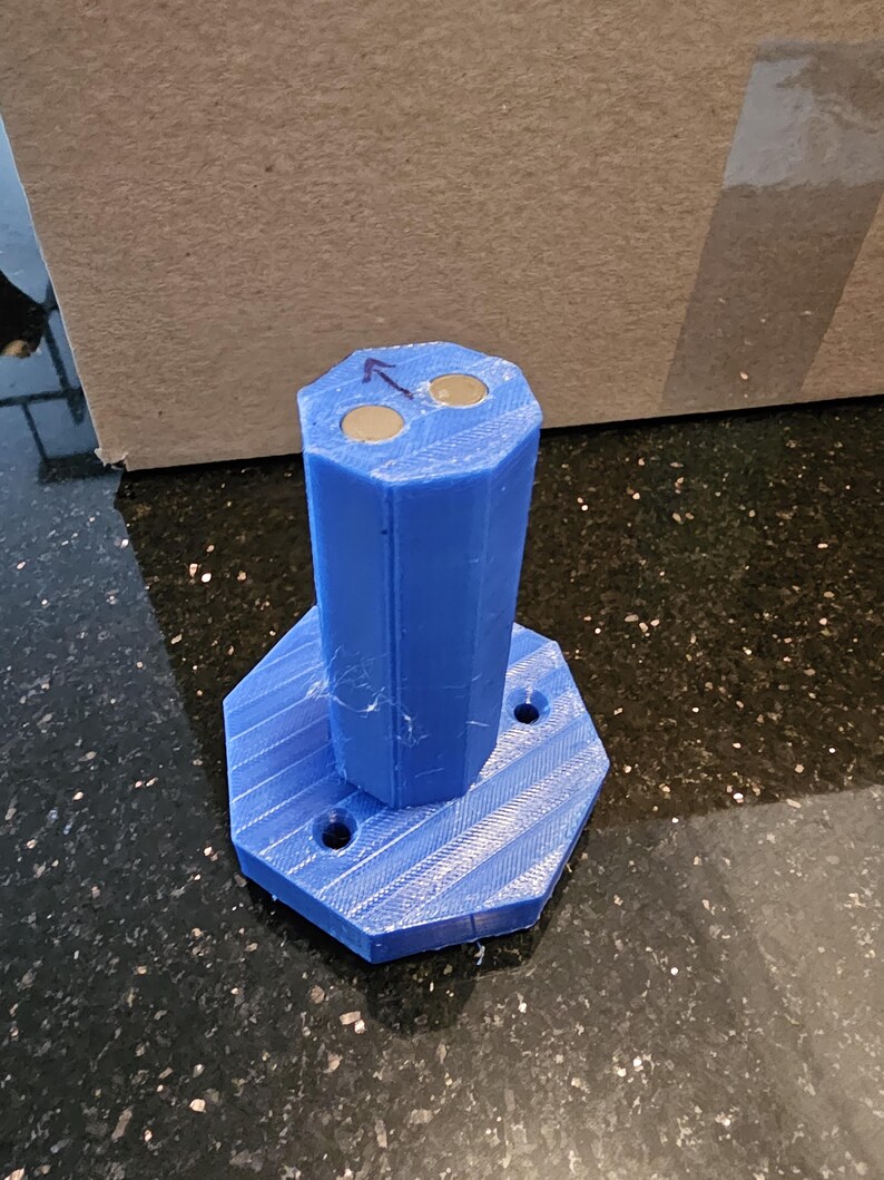 May include: A blue 3D printed octagonal base with three holes and a blue 3D printed cylinder with two round magnets on top.