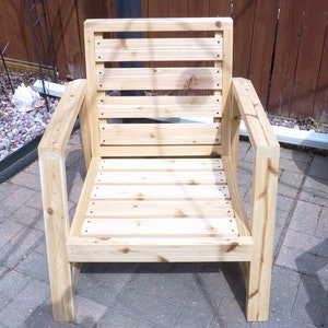 K&ouml;nnte beinhalten: Ein Holzstuhl mit einer Lattenr&uuml;cklehne und einem Latten-Sitz. Der Stuhl ist aus unbehandeltem Holz und hat ein schlichtes, modernes Design.