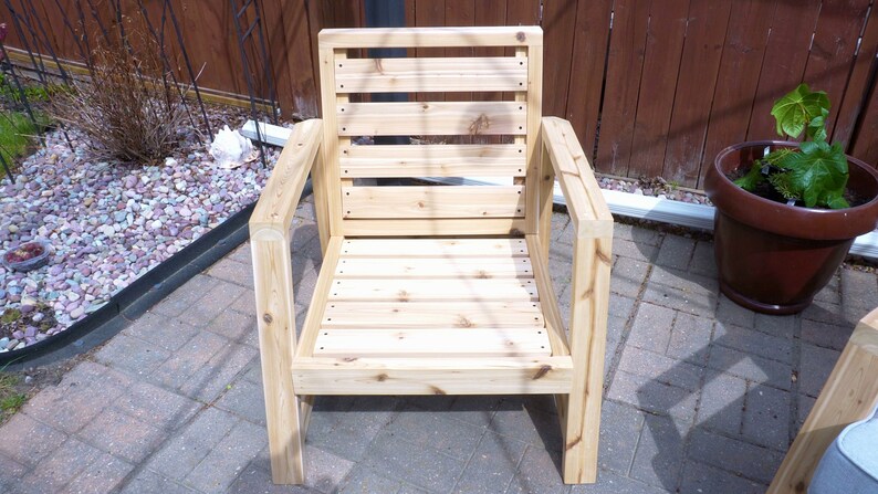 K&ouml;nnte beinhalten: Ein Holzstuhl mit einer Lattenr&uuml;cklehne und einem Latten-Sitz. Der Stuhl ist aus unbehandeltem Holz und hat ein schlichtes, modernes Design.