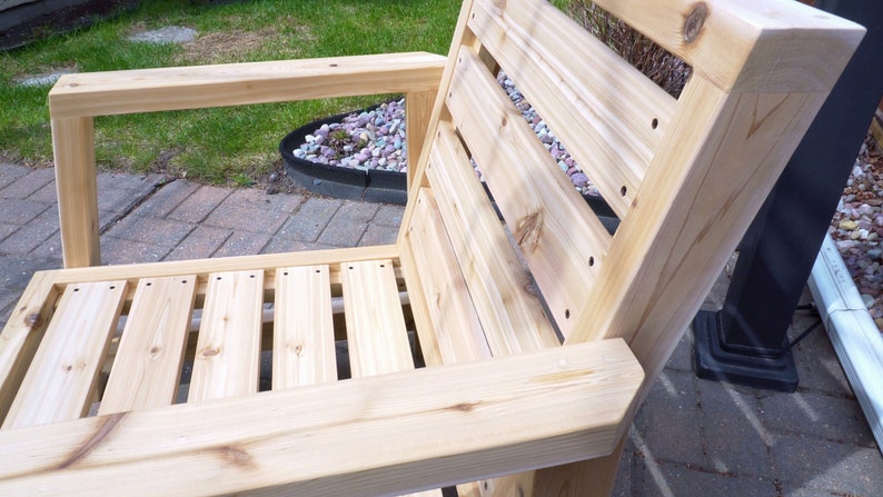 K&ouml;nnte beinhalten: Ein Holzstuhl mit einer Lattenr&uuml;cklehne und einem Latten-Sitz. Der Stuhl ist aus unbehandeltem Holz und hat eine nat&uuml;rliche Farbe.