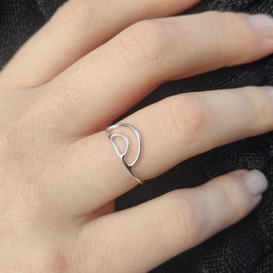 Könnte beinhalten: Ein silberner Ring mit einem Doppelkreis-Design. Der Ring wird am Finger einer Person getragen.