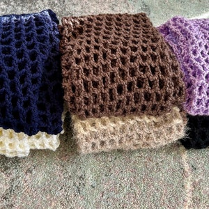 May include: A collection of five folded crochet items featuring an open, grid-like stitch pattern. The colors include dark navy blue, cream, brown, beige, lavender, and black, all stacked in a neat arrangement to display the varied yarn textures.