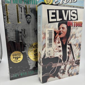 May include: Two Elvis Presley commemorative VHS tapes. One tape is titled "The Great Performances" with a black and white image of Elvis. The other tape is titled "Elvis On Tour" with a color image of Elvis playing guitar.
