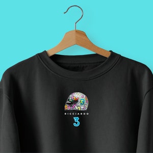 May include: Black sweatshirt featuring a colourful graphic of a racing helmet and the text "RICCIARDO 3" printed on the front.