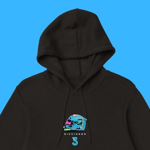 Può includere: Felpa con cappuccio nera con una grafica di un casco da corsa blu e rosa con il numero 3 e il testo "RICCIARDO" stampato sul davanti.